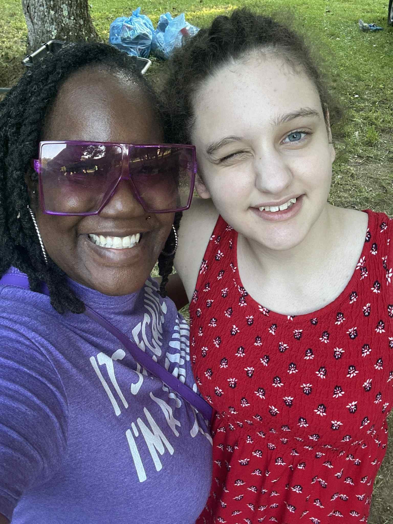 Smiling together — big pink sunglasses and a red floral dress — Campout 2025