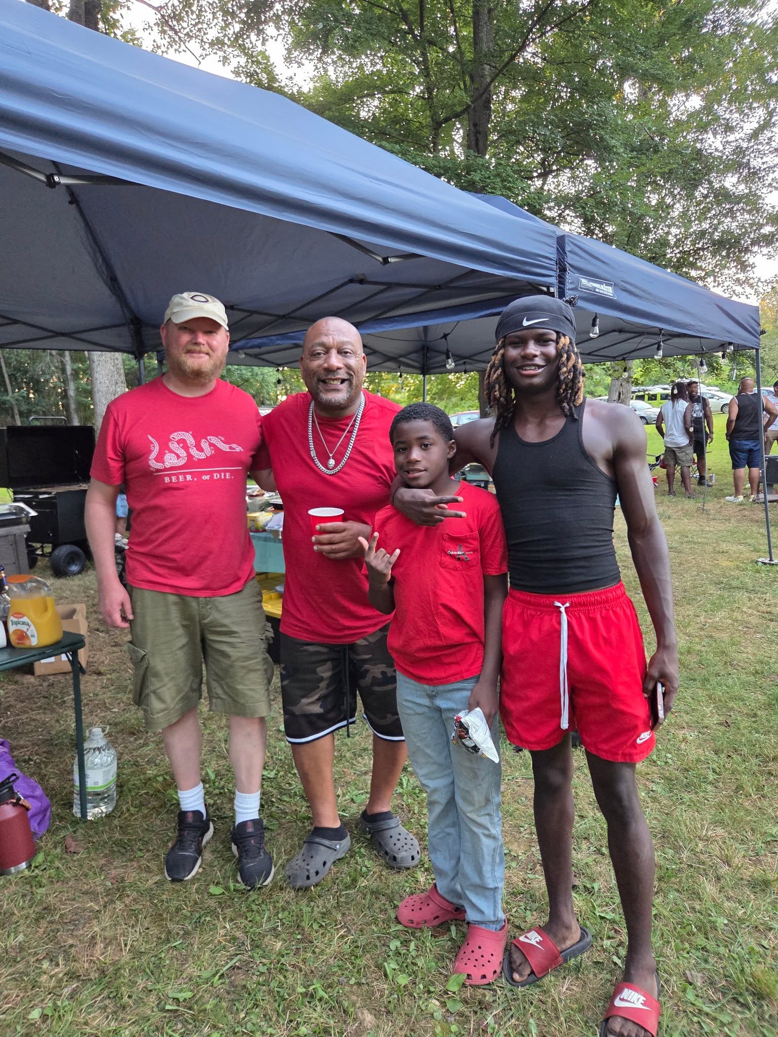 Guests in matching red shirts posing under the food tent at dusk — Campout 2025