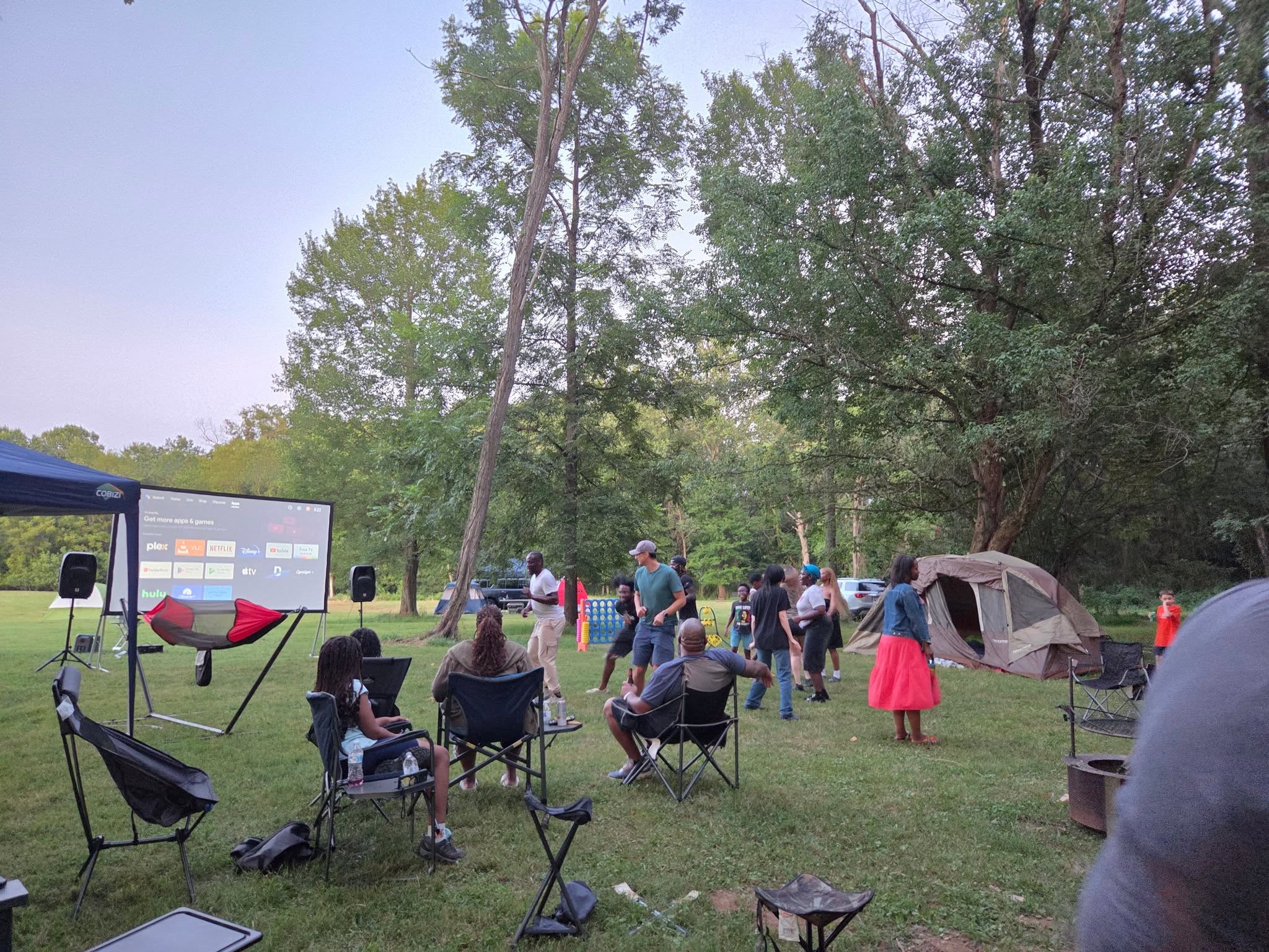 Outdoor movie screen glowing at dusk with guests in camp chairs — Campout 2025