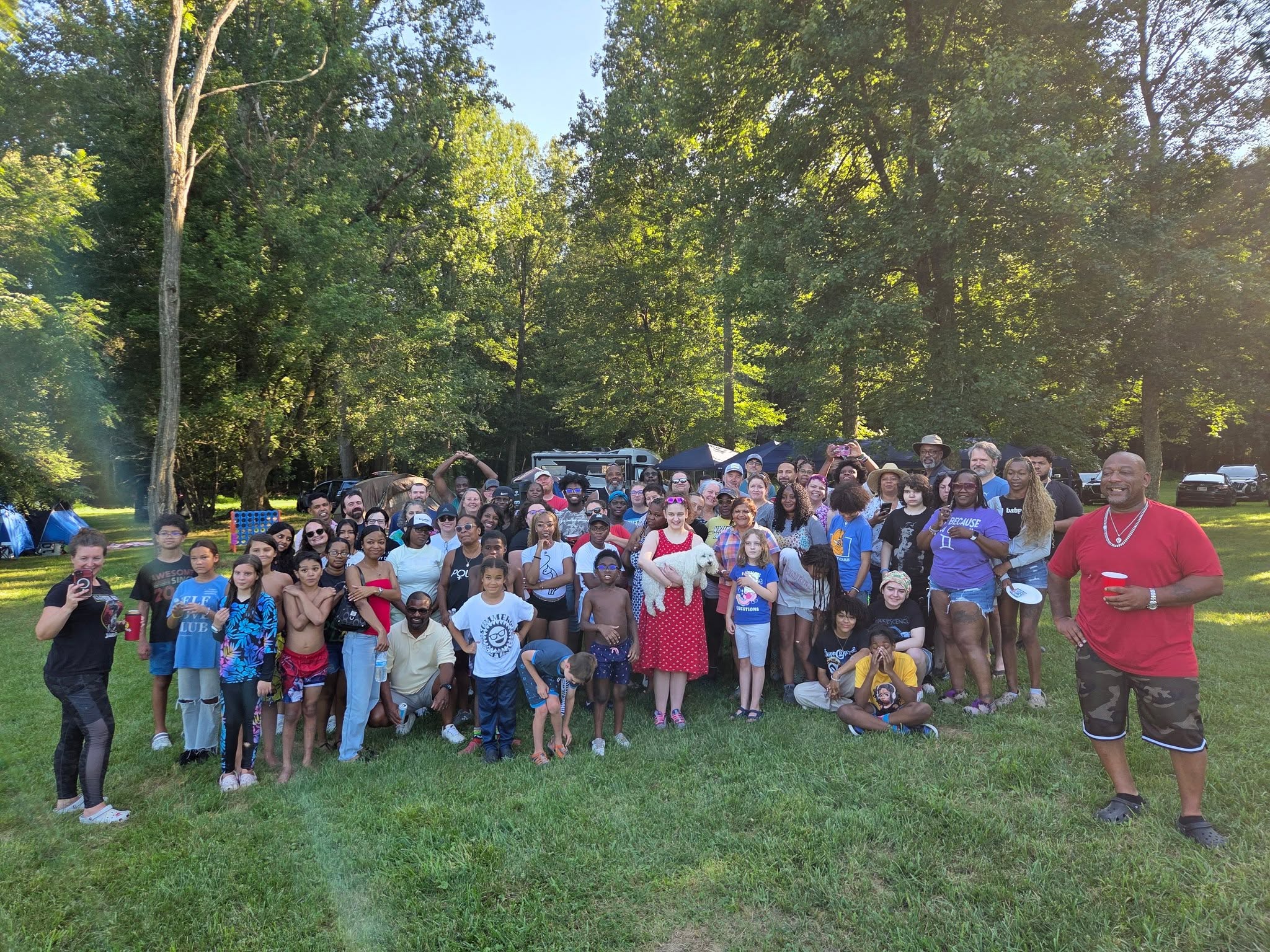 Wide group shot of guests gathered on the grassy lawn at sunset — Campout 2025